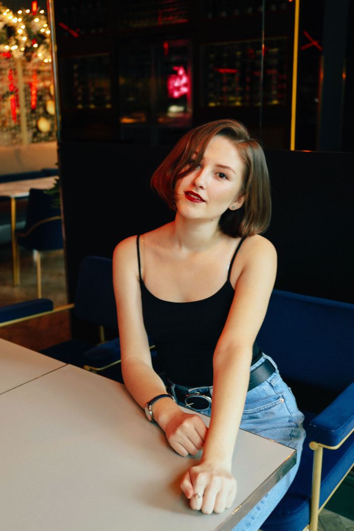 Stylish young woman sitting in a cafe, wearing a black tank top, looking confidently at the camera.